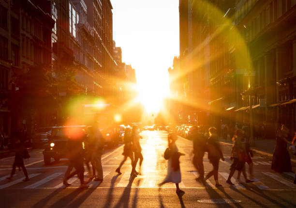 People walking across the street in New York City with the bright light of sunset shining between the buildings along 23rd St in Midtown Manhattan NYC